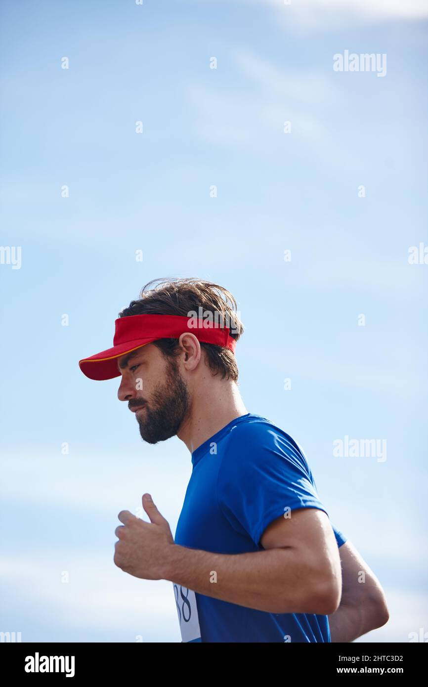 Hes in the zone. Shot of a young man running a marathon with the sky as background. Stock Photo