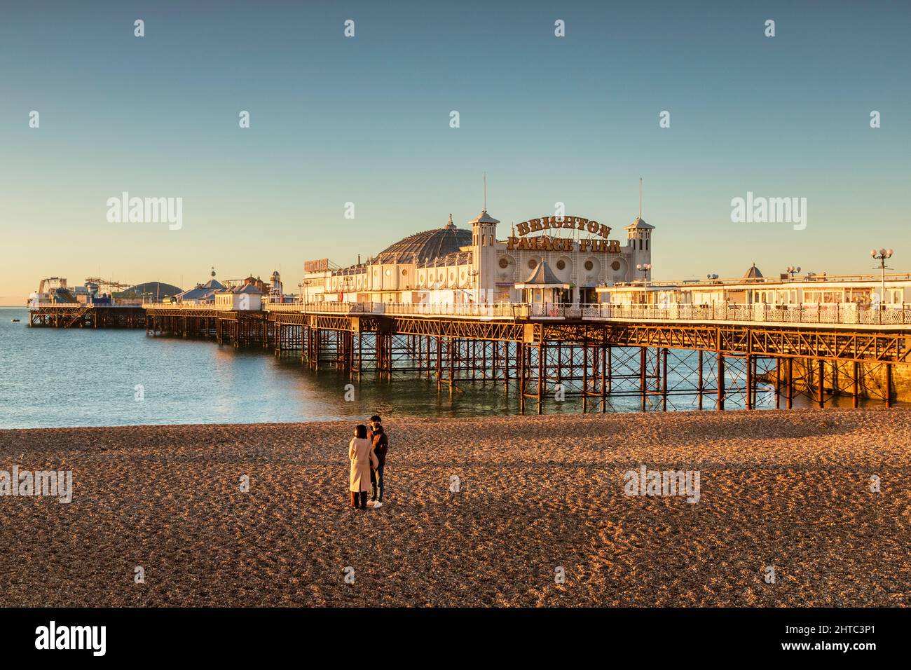 14 January 2022: Brighton, East Sussex, UK - Sunrise at Brighton Palace Pier, with young couple on beach. Stock Photo