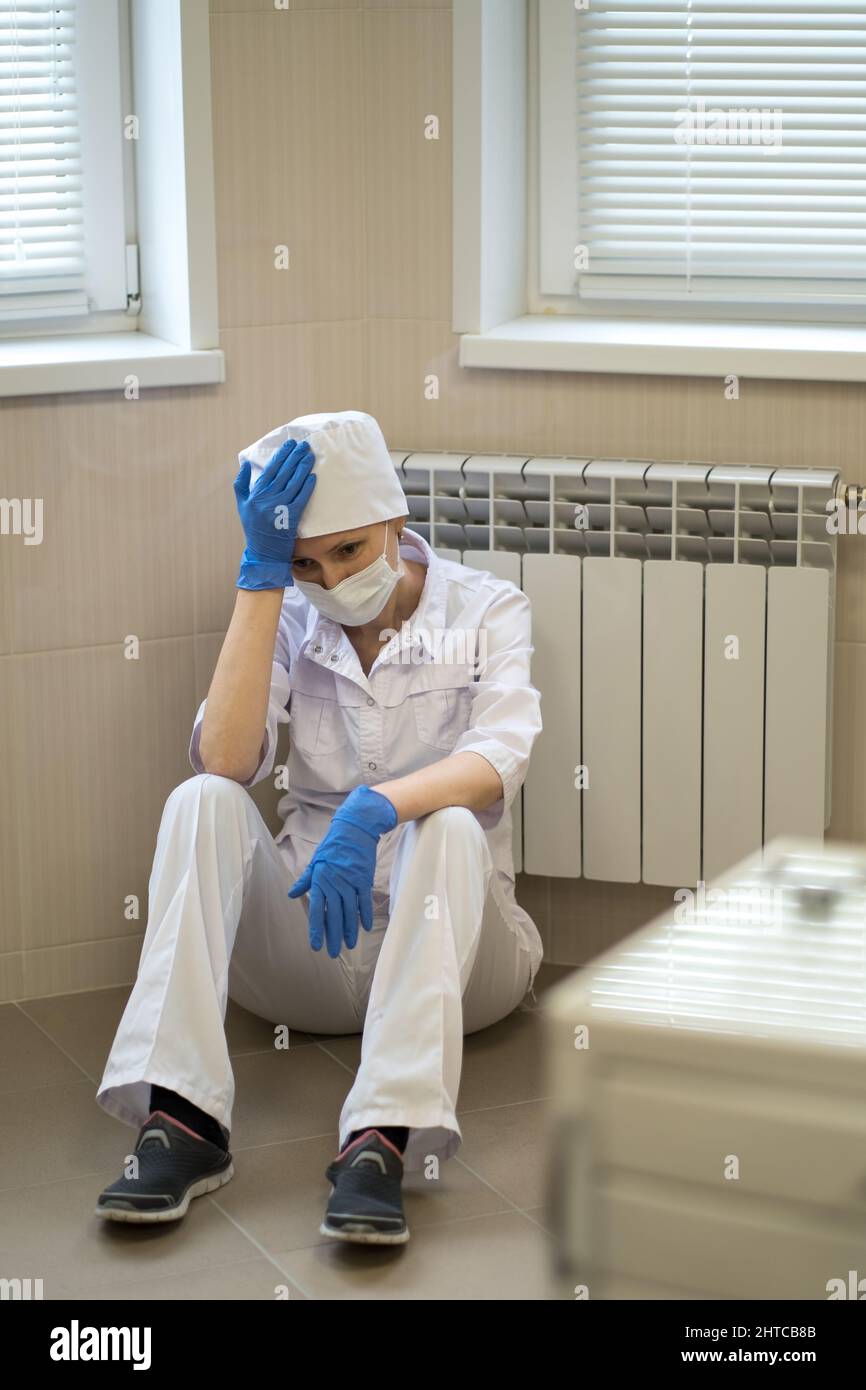 A female doctor sits tiredly on the hospital floor. Stock Photo