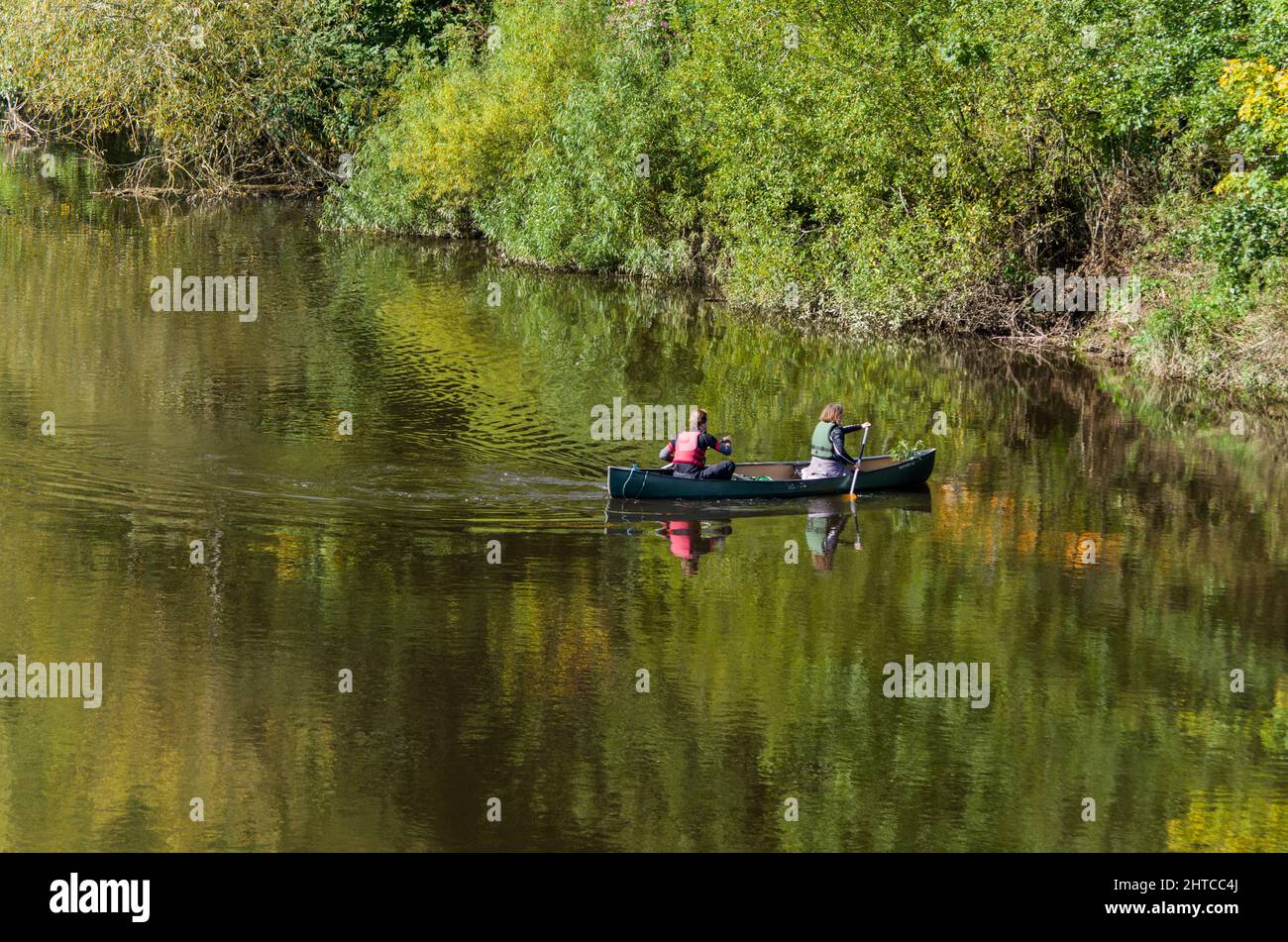 The still waters of the River Wye near Whitney On Wye, Herefordshire, UK; two people in a canoe Stock Photo