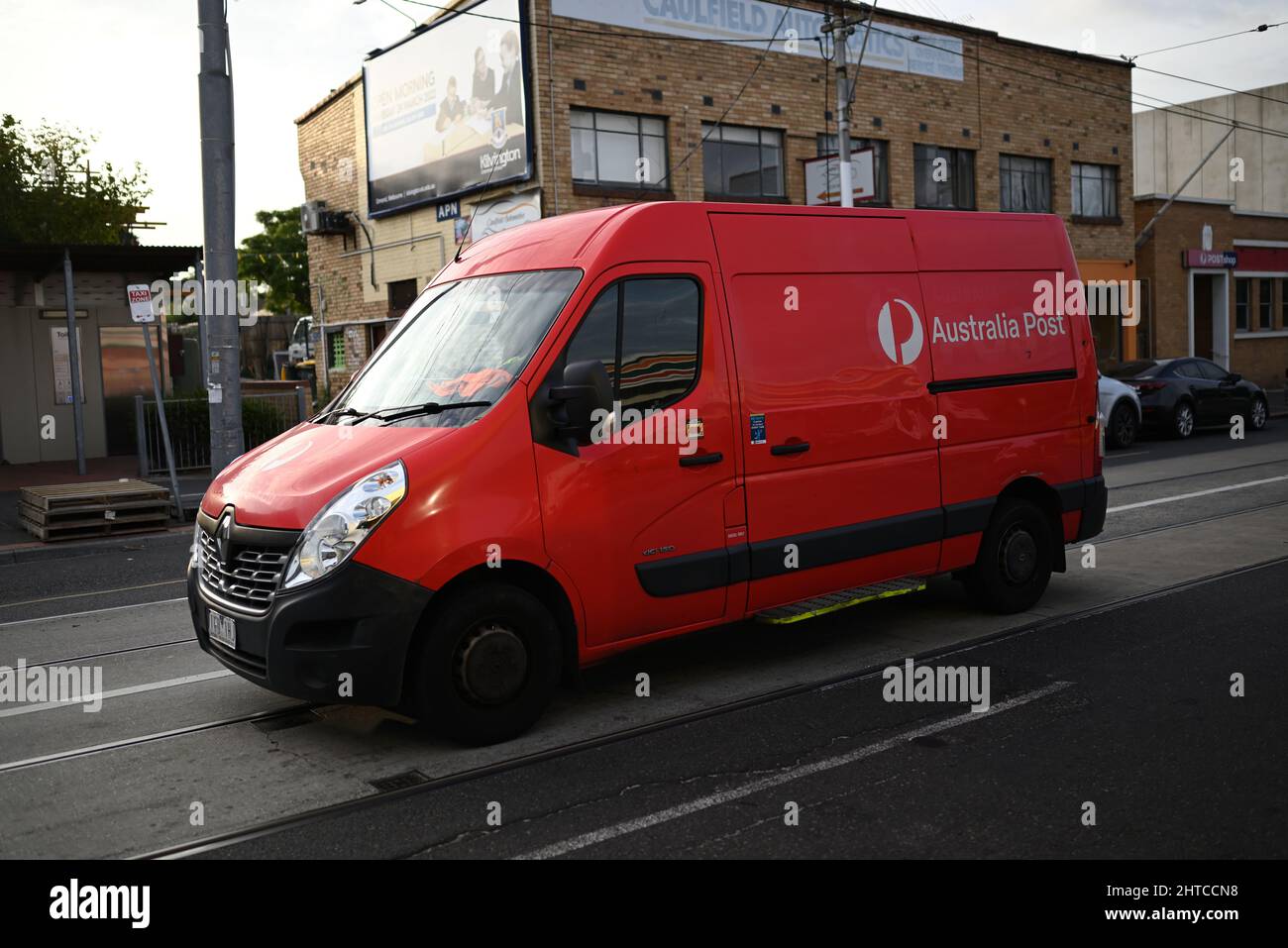 Red Australia Post van, a Renault Master, travelling along Hawthorn Rd at dusk. Shops, including a Post Shop, can be seen in the background Stock Photo