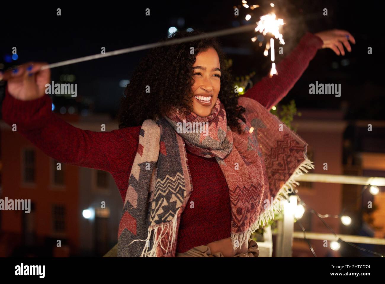 Confident multi-racial young adult female dancing while holding a sparkler on rooftop terrace. Good times, night life in the city. Stock Photo