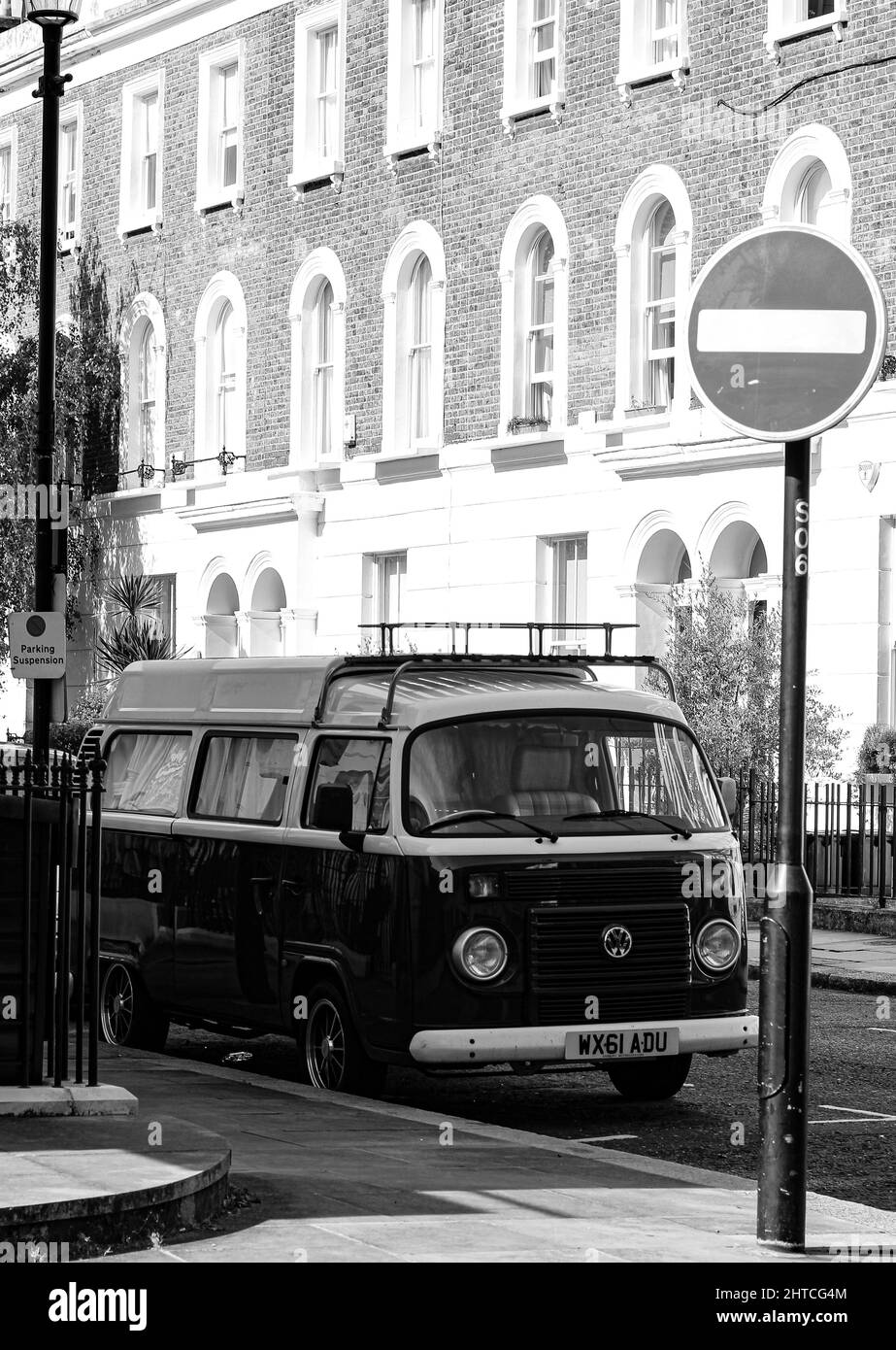 Vertical grayscale shot of a VW van parked near a stop sign in the Chelsea district, London, the UK Stock Photo