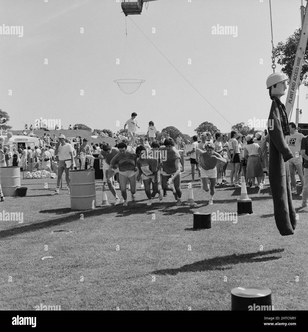 Laing Sports Ground, Rowley Lane, Elstree, Barnet, London, 21/06/1986. A team in the 'It's a Knockout' style competition at the 1986 Family Day at Laing's Sports Ground running towards the camera with the effigy of a builder from the 'swinging dummy' stage hanging on the right. Over 2500 people attended the Family Day and raised over &#xa3;700 for that year's designated charity The British Heart Foundation.  Attractions included; guest appearances by the cast of the television programme Grange Hill, a bouncy castle, donkey rides, Punch and Judy shows, Pierre the Clown, children's races, blindf Stock Photo