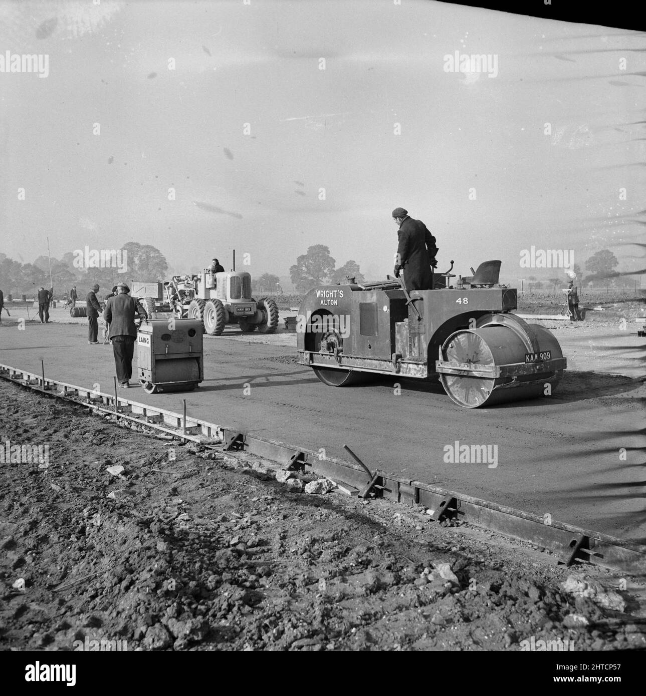 RAF Gaydon, Gaydon, Stratford-on-Avon, Warwickshire, 11/10/1952. Work underway on the construction of a new runway at Gaydon Airfield, showing a Wright's roller and a pedestrian roller compacting the concrete working course. Work began on the construction of a runway at Gaydon Airfield in early 1952. As part of the project, a former runway, largely abandoned following the Second World War, was superseded by a newly constructed runway nearly 1 3/4 miles long and 200 feet wide. Also built were access tracks and a taxi-track. The runway was constructed on 8 inches of hardcore, with four inches of Stock Photo