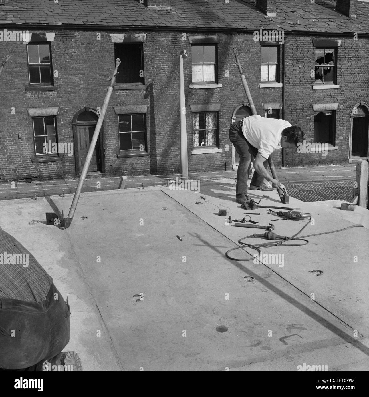 St Mary's Estate, Oldham, 01/09/1964. A worker securing a concrete slab during the construction of 12M Jespersen prototype flats in Oldham, with derelict terraced houses in the background. In 1963, John Laing and Son Ltd bought the rights to the Danish industrialised building system known as Jespersen (sometimes referred to as Jesperson). The company built factories in Scotland, Hampshire and Lancashire producing Jespersen prefabricated parts and precast concrete panels, allowing the building of housing to be rationalised, saving time and money. The prototype flats shown in the photograph were Stock Photo
