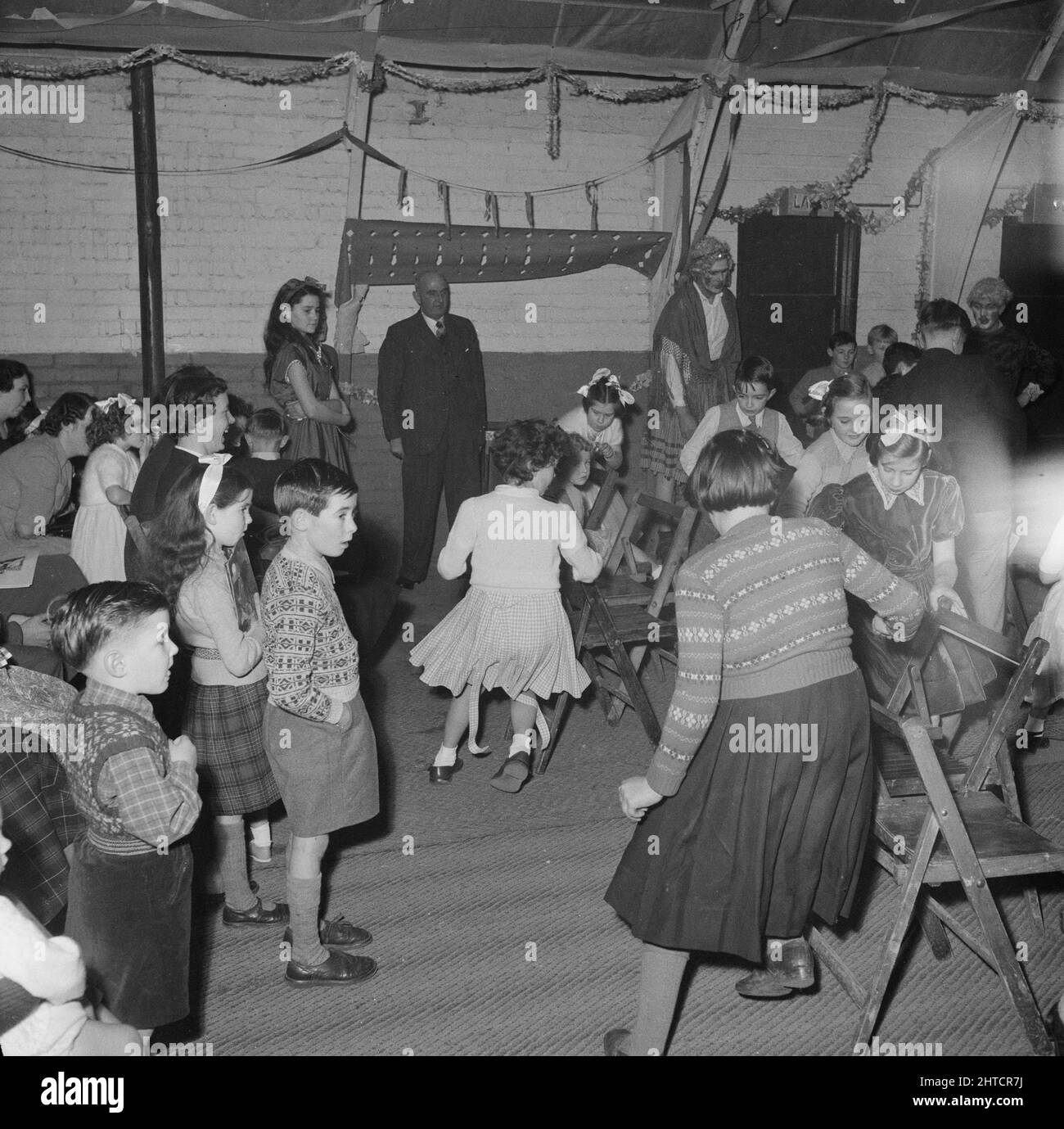 Thurleigh Airfield, Thurleigh, Bedfordfordshire, 19/12/1953. A game of musical chairs being played at a children's party. This photograph shows a children's party that was organised by Laing's Welfare staff and members of the Committee for the children of staff working on the Thurleigh Airfield project. The party was held in the Camp Theatre and included clowns, games, a film show, presents from Santa Claus and tea for sixty children. Stock Photo