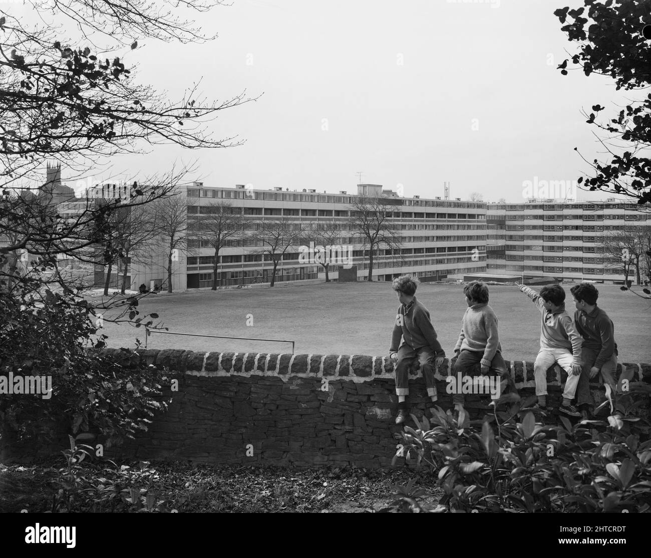 Victoria Park Estate, Macclesfield, Cheshire East, Cheshire, 18/04/1968. Four boys sitting on a stone wall, looking towards flats in the distance at the Victoria Park development, built using the 12M Jespersen system. In 1963, John Laing and Son Ltd bought the rights to the Danish industrialised building system for flats known as Jespersen (sometimes referred to as Jesperson). The company built factories in Scotland, Hampshire and Lancashire producing Jespersen prefabricated parts and precast concrete panels, allowing the building of housing to be rationalised, saving time and money. The Victo Stock Photo