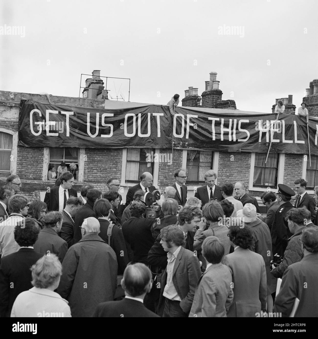 Westway Flyover, A40, Kensington and Chelsea, London, 28/07/1970. A crowd gathered beside a journalist interviewing Michael Heseltine at the opening of the Westway Flyover, with a protest banner draped in the background. Michael Heseltine was Parliamentary Secretary to the Ministry of Transport, and deputised for the Minister John Peyton to cut the tape for the opening of the Westway Flyover. Acklam Road was the focus of protests against the Westway by local residents. Houses along one side of the street had been demolished to make way for the flyover. At a reception held earlier that day at t Stock Photo