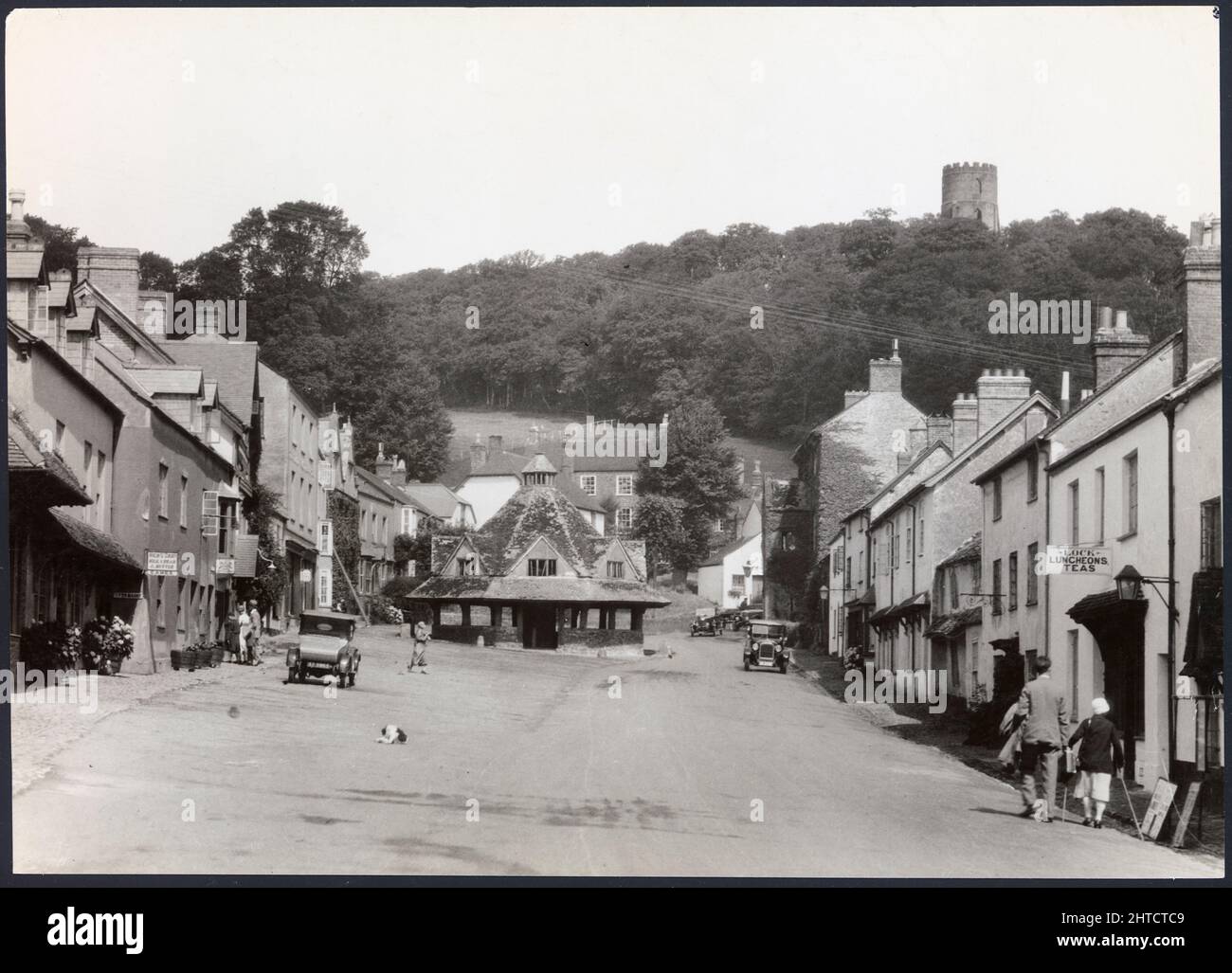 Yarn Market, High Street, Dunster, Somerset, 1925-1935. A view looking north along Dunster High Street towards the Yarn Market with Conygar Tower on the hillside in the distance. During the medieval period Dunster became a centre for woollen production but by the 15th century it's significance was beginning to decline. The Yarn Market is believed to date from c1609 and was constructed by George Luttrell as a means to stem this decline and maintain the importance of Dunster as a market town. The folly Conygar Tower was built in 1775 for Henry Fownes Luttrell (c1722-1780), who became legal owner Stock Photo