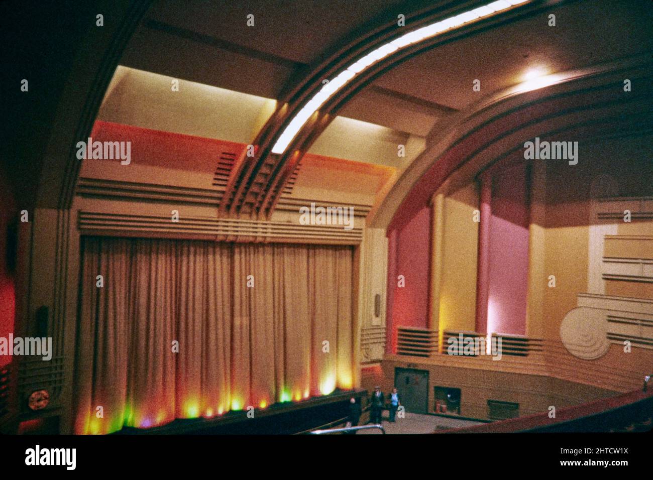Odeon Cinema, Fortis Green Road, Muswell Hill, Haringey, London, 1974-1999. The auditorium in the Odeon Cinema, viewed from the side of the circle, showing the curtained screen, proscenium and curved front and ceiling. The Odeon Cinema opened in 1936. The exterior design of the building was restricted and subdued due to opposition from the church located opposite; the interior was therefore designed to compensate. The auditorium is described as being &quot;the most elaborate interior of any Odeon cinema to survive&quot;. It was divided into three screens in 1974, with two screens in beneath th Stock Photo