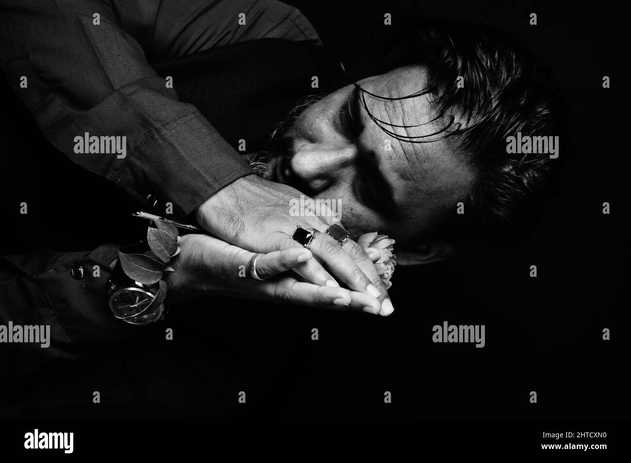 Grayscale portrait of a somber bearded South Asian man, with flower in clasped hands Stock Photo