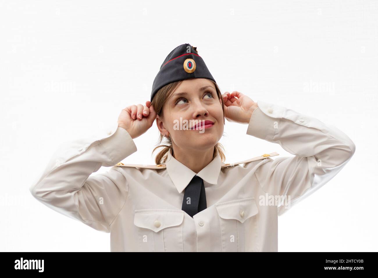 A beautiful young female Russian police officer in dress uniform in a cap and a white shirt smiles on a white background. Selective focus. Portrait Stock Photo