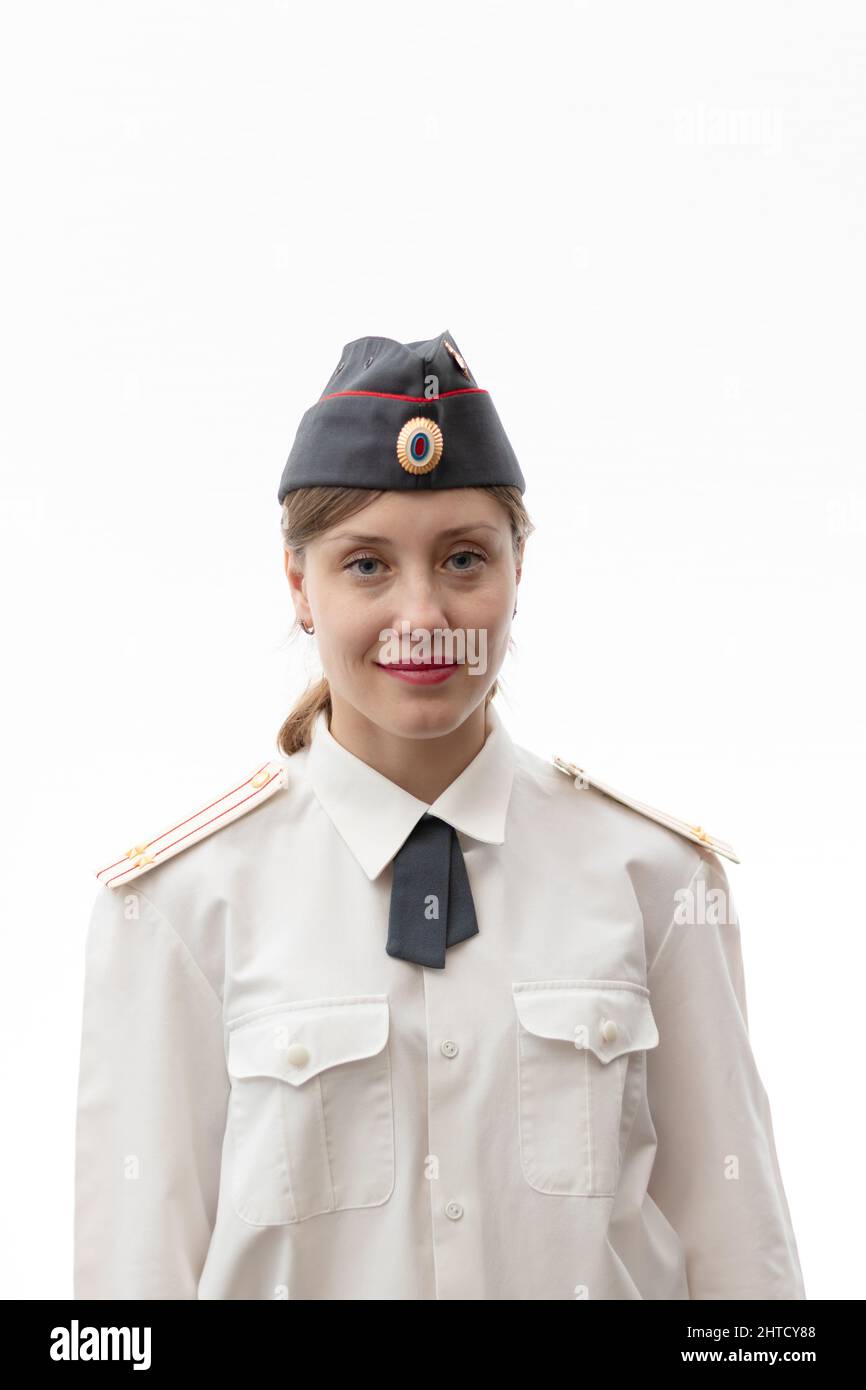 A beautiful young female Russian police officer in dress uniform in a cap and a white shirt smiles on a white background. Selective focus. Portrait Stock Photo