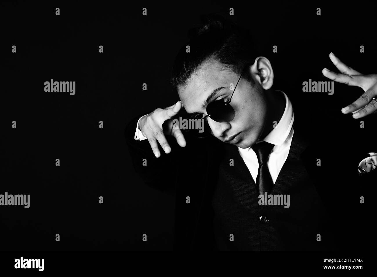 A grayscale portrait of a hip young South Asian man in a suit with random hand gesture against a dark background Stock Photo