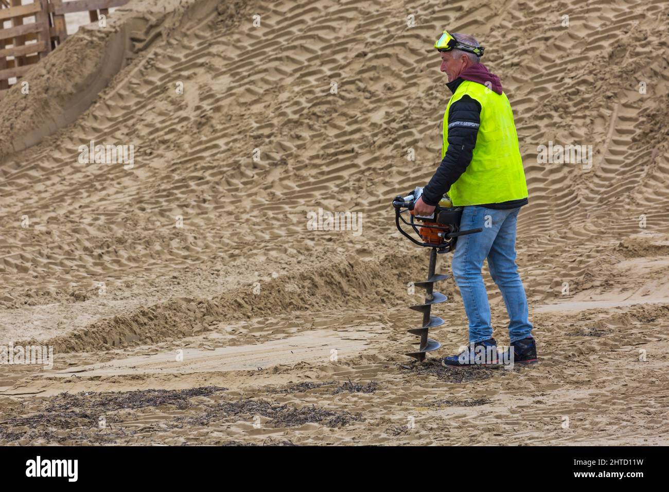 Man in high vis vest drilling holes for posts in preparations of course at motocross racing event on Weymouth beach, Weymouth, Dorset UK in October Stock Photo