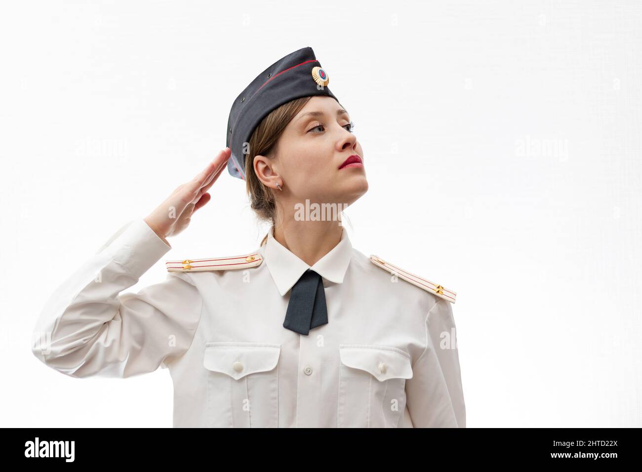 A beautiful young female Russian police officer in dress uniform and a white shirt on a white background salutes the commander. Selective focus. Portr Stock Photo