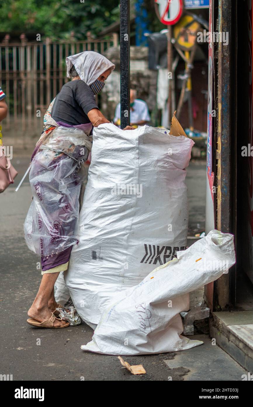 A vertical shot of a poor old lady finding plastic in the trash bag in