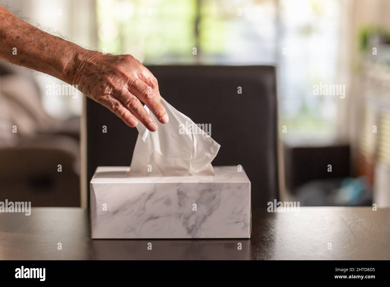 Senior man hand picking up tissue paper from tissue box on dinner table. Stock Photo