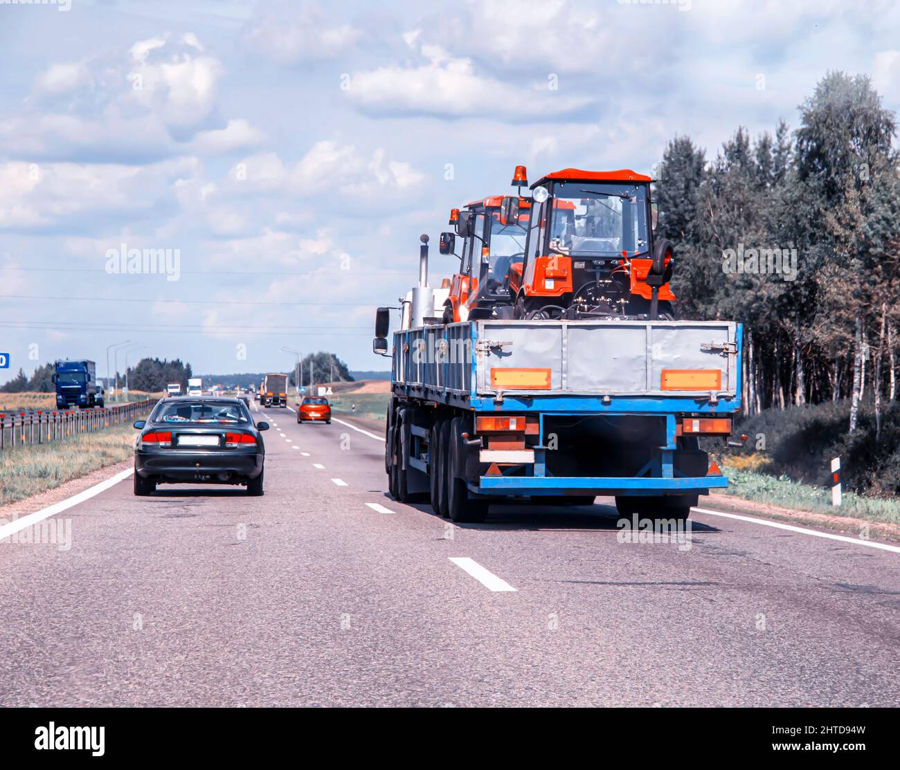 Transporting new tractors in a truck trailer on the road. Oversized cargo transportation, industry Stock Photo