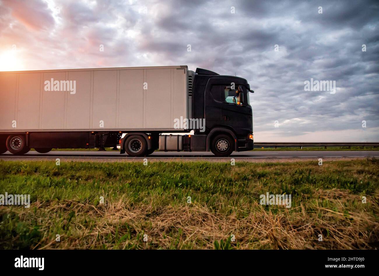 A modern truck with a semitrailer refrigerator transports cargo against the backdrop of a cloudy sky with clouds. Transportations carried out by road Stock Photo