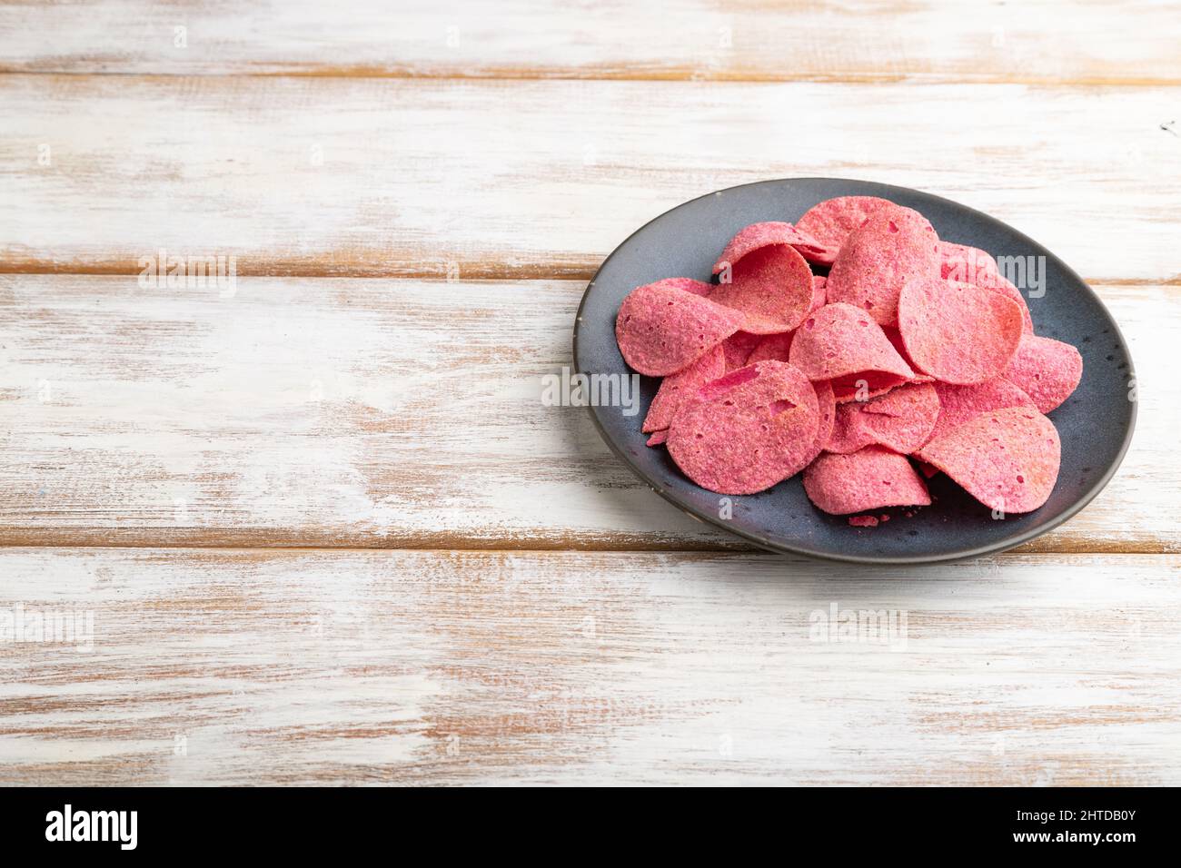 red potato chips with herbs and tomatoes on white wooden background