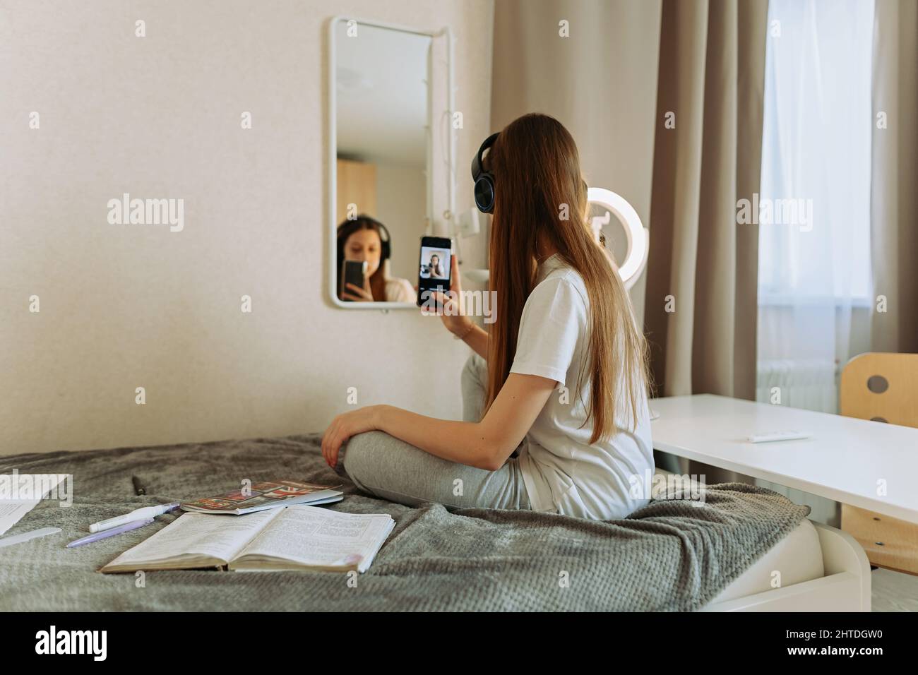 Teenage girl in headphones in front of the mirror takes selfie, admires. Reflection Stock Photo