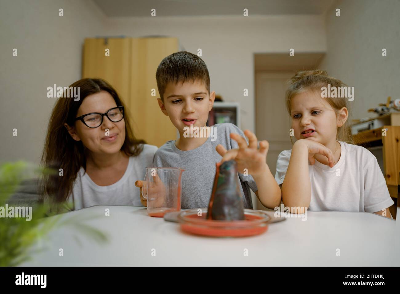 Mom and children at home are conducting an experiment with volcanic eruption. Stock Photo