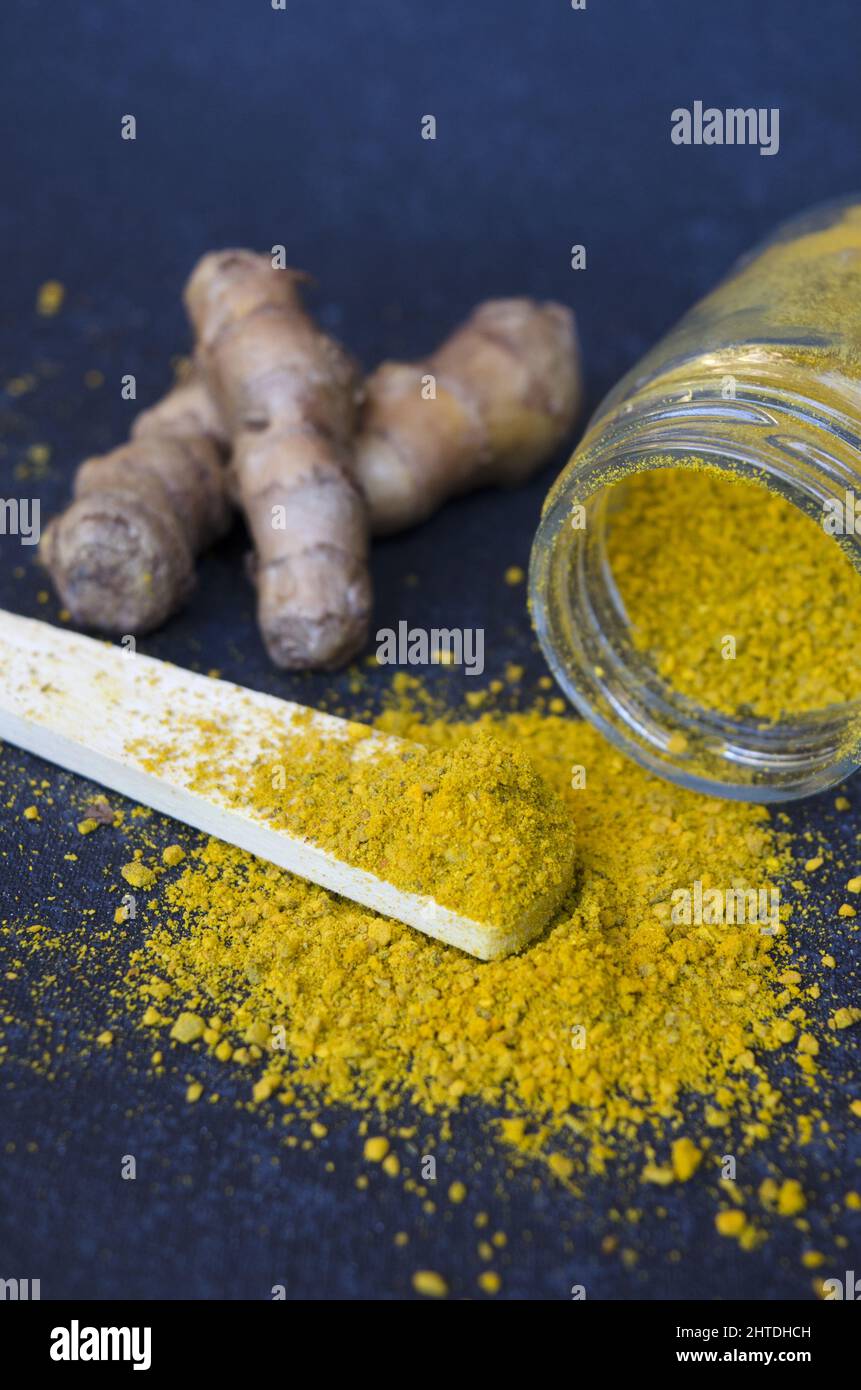 Vertical shot of turmeric jar and roots with a wooden spoon on a dark blue background Stock Photo