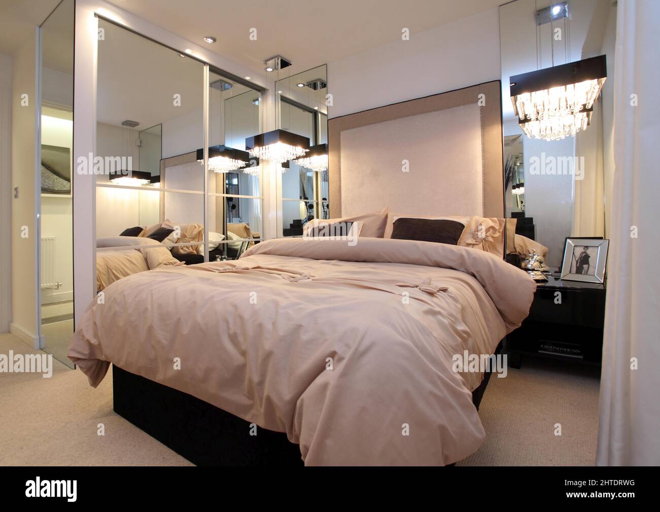 Modern bedroom in new build home,bedspread,padded headboard, mirror mirrored wardrobes,beige white cream neutral colour scheme, large mirrors increase Stock Photo