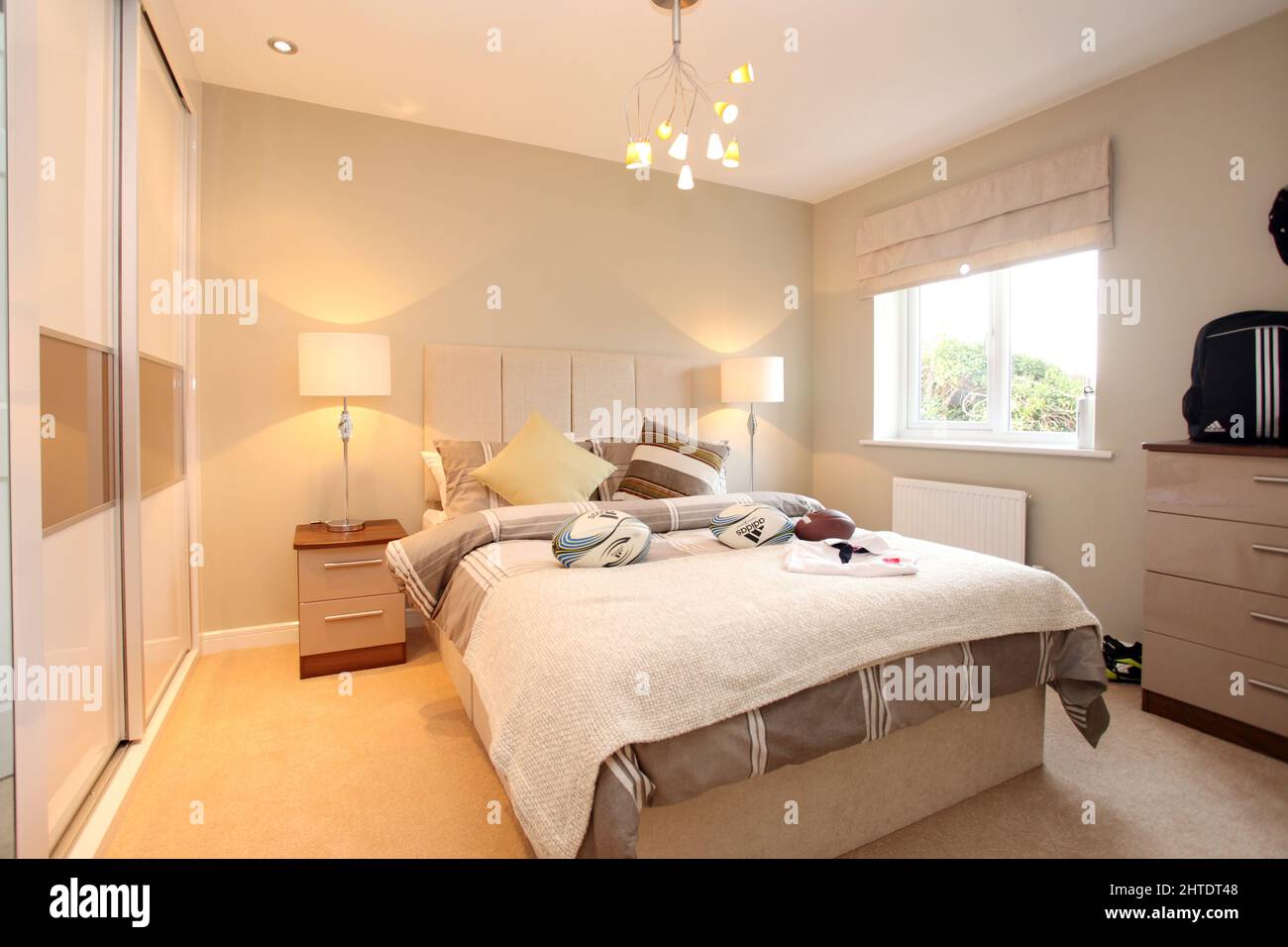 Modern boys bedroom in new build home, rugby theme, bedspread,beige neutral colour scheme,tall padded feature headboard,rugby balls, boys bedroom, Stock Photo