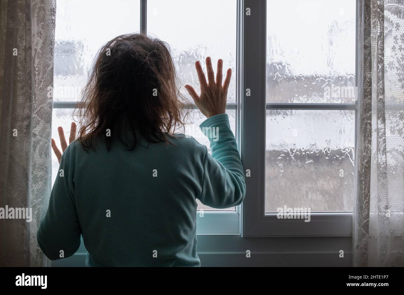 Woman looking out of window on rainy day. Conept image; female depression, domestic abuse, human trafficking, domestic violence, mental health... Stock Photo
