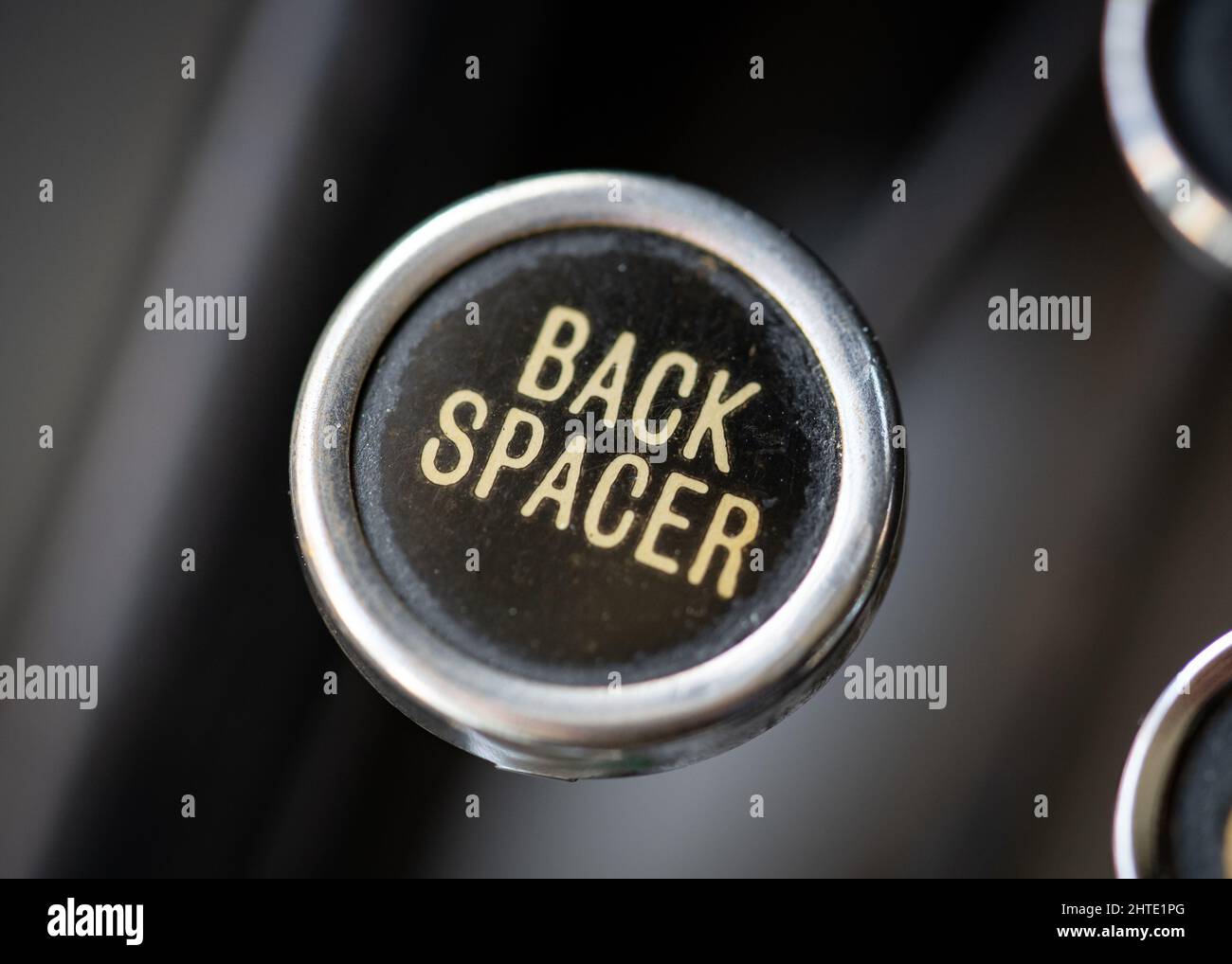 Retro vintage back spacer typewriter circular round key closeup with gold coloured back space key on black background. Stock Photo
