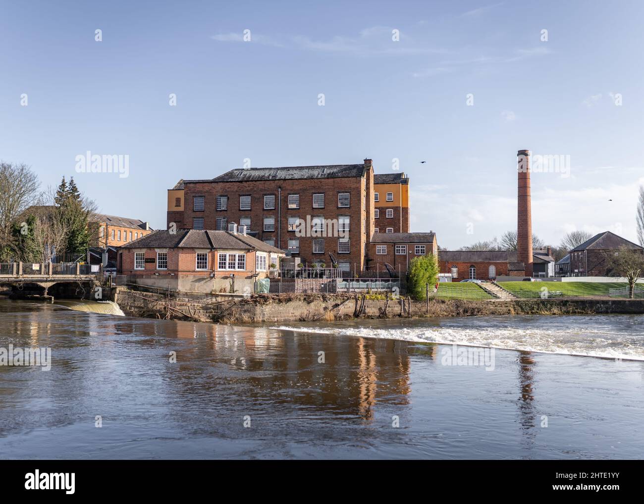 The West Mill on the river Derwent at Derby Abby. Fast flowing beautiful river and old mill warehouse with red brick chimney. Stock Photo