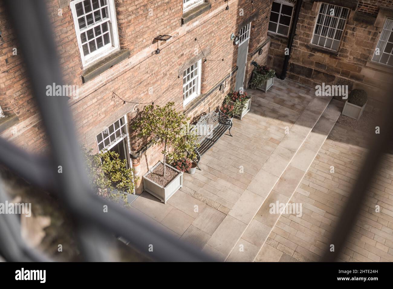 Old mill warehouse red brick courtyard with bench and trees on summer day. Looking out of old wooden sash window. Stock Photo