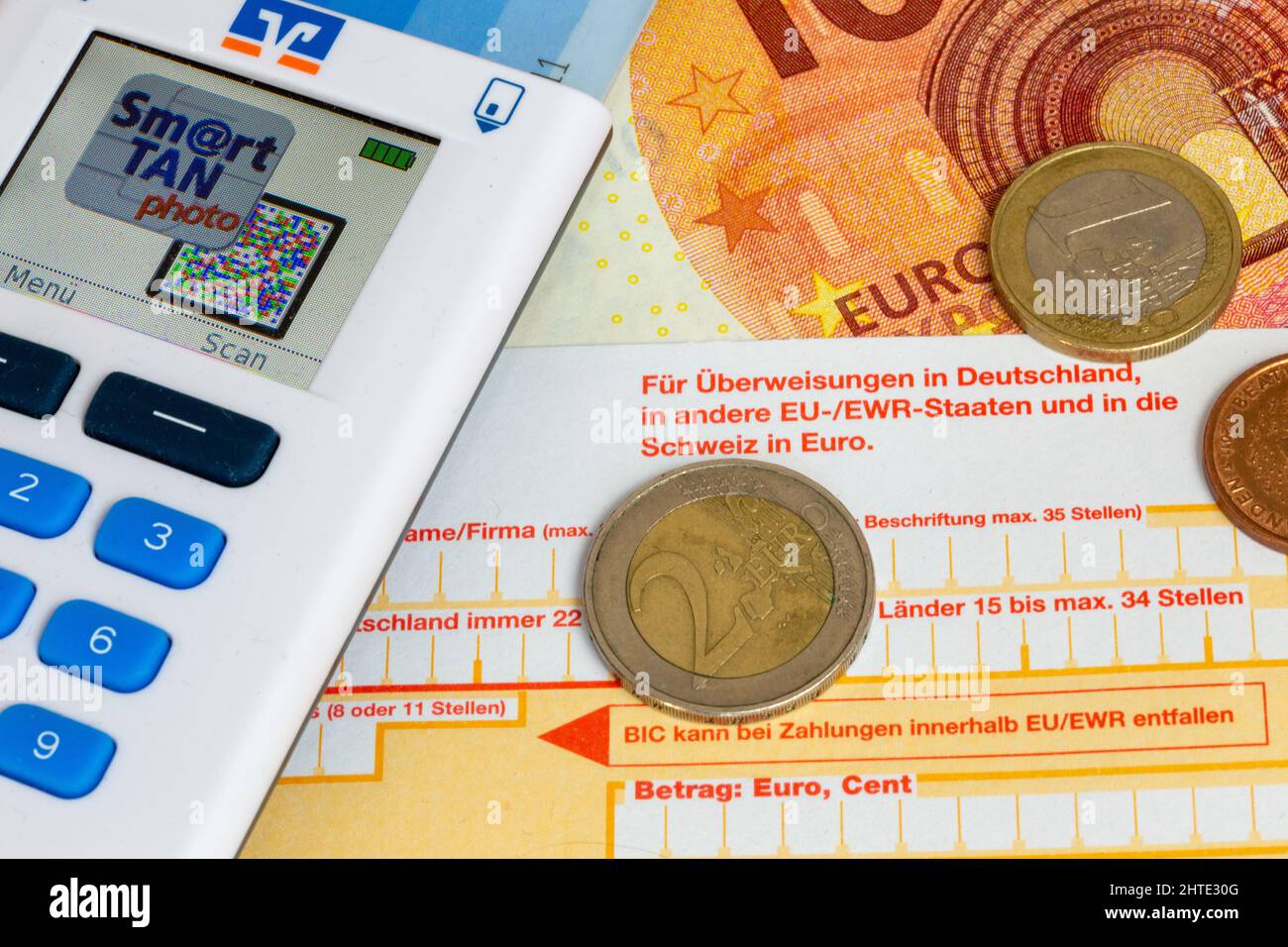 Symbol image of payment transactions: Close-up of a bank transfer slip with Euro coins, Euro bills and TAN generator Stock Photo