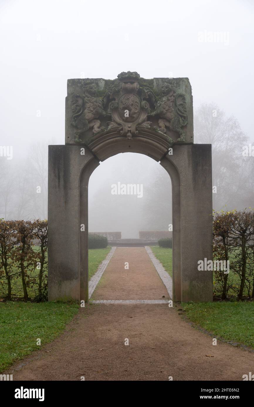 Vertical shot of a gorgeous stone arch at the Palais Rosenhoehe Darmstadt park surrounded by fog Stock Photo