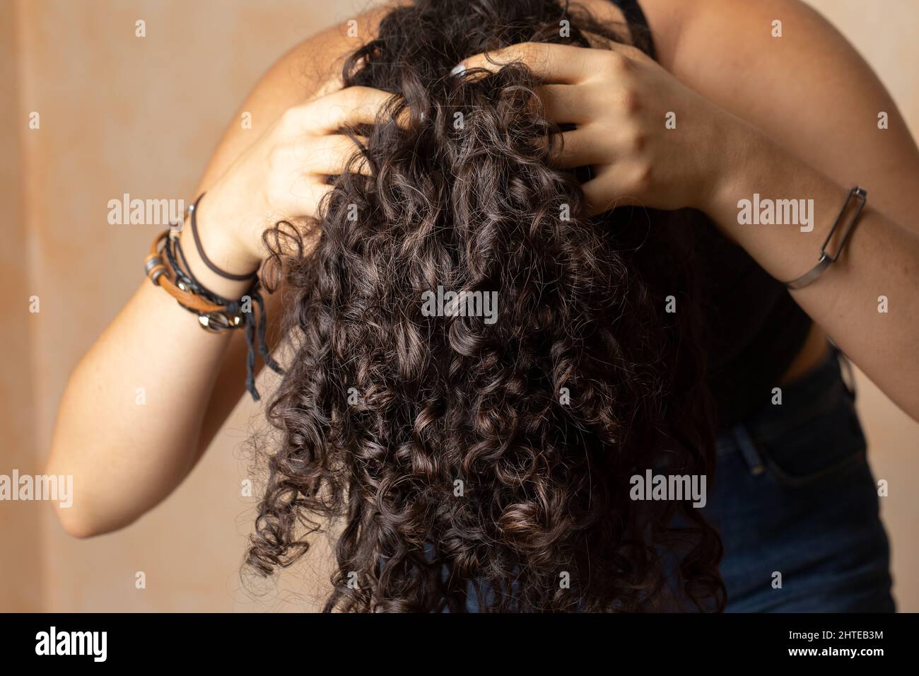 Young woman with long curly hair giving herself a scalp massage as part
