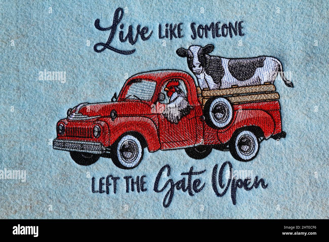 machine embroidery,text, Live like someone left the gate open, words, red farm truck, rooster driving, cow riding, humorous, blue felt fabric, texture Stock Photo