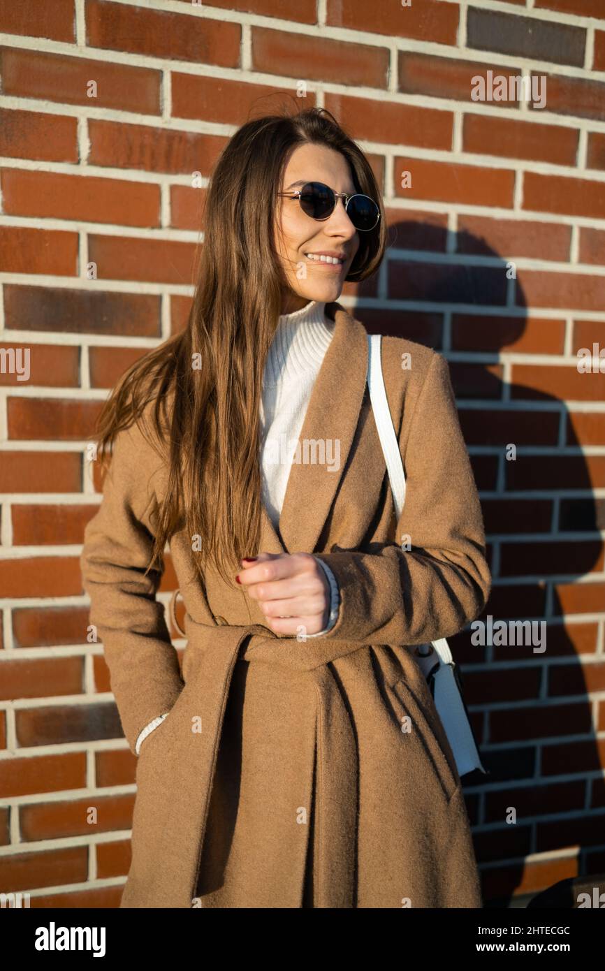 Positive young woman in a brown coat and sunglasses on the background ...