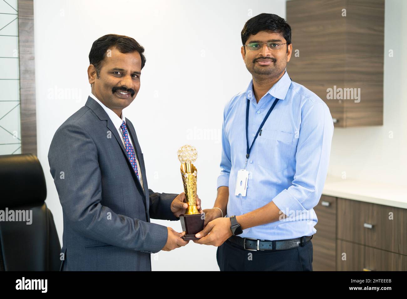 Young corporate employee receiving trophy from boss in office concept
