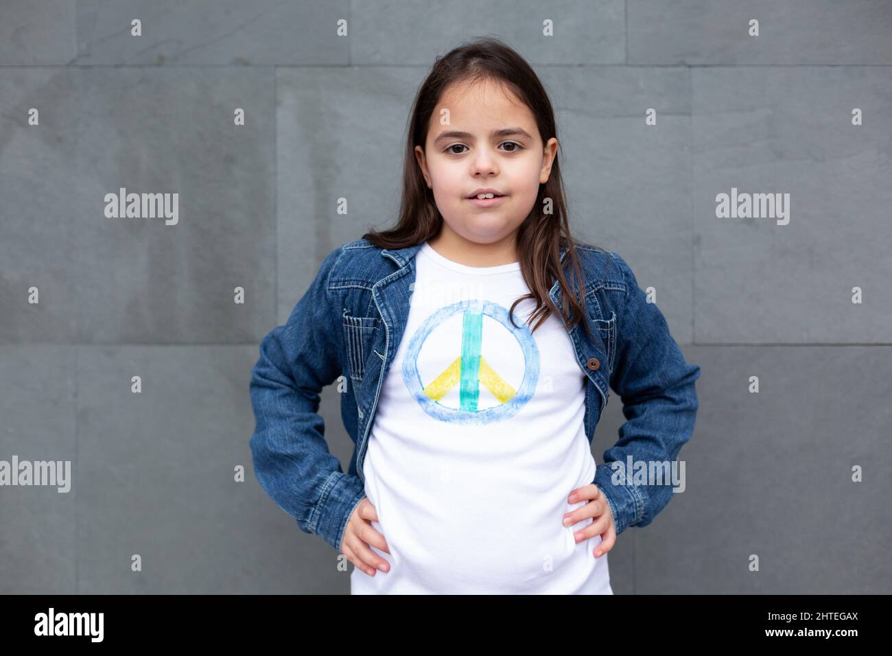 Little girl showing peace symbol t-shirt isolated on grey wall. Stock Photo