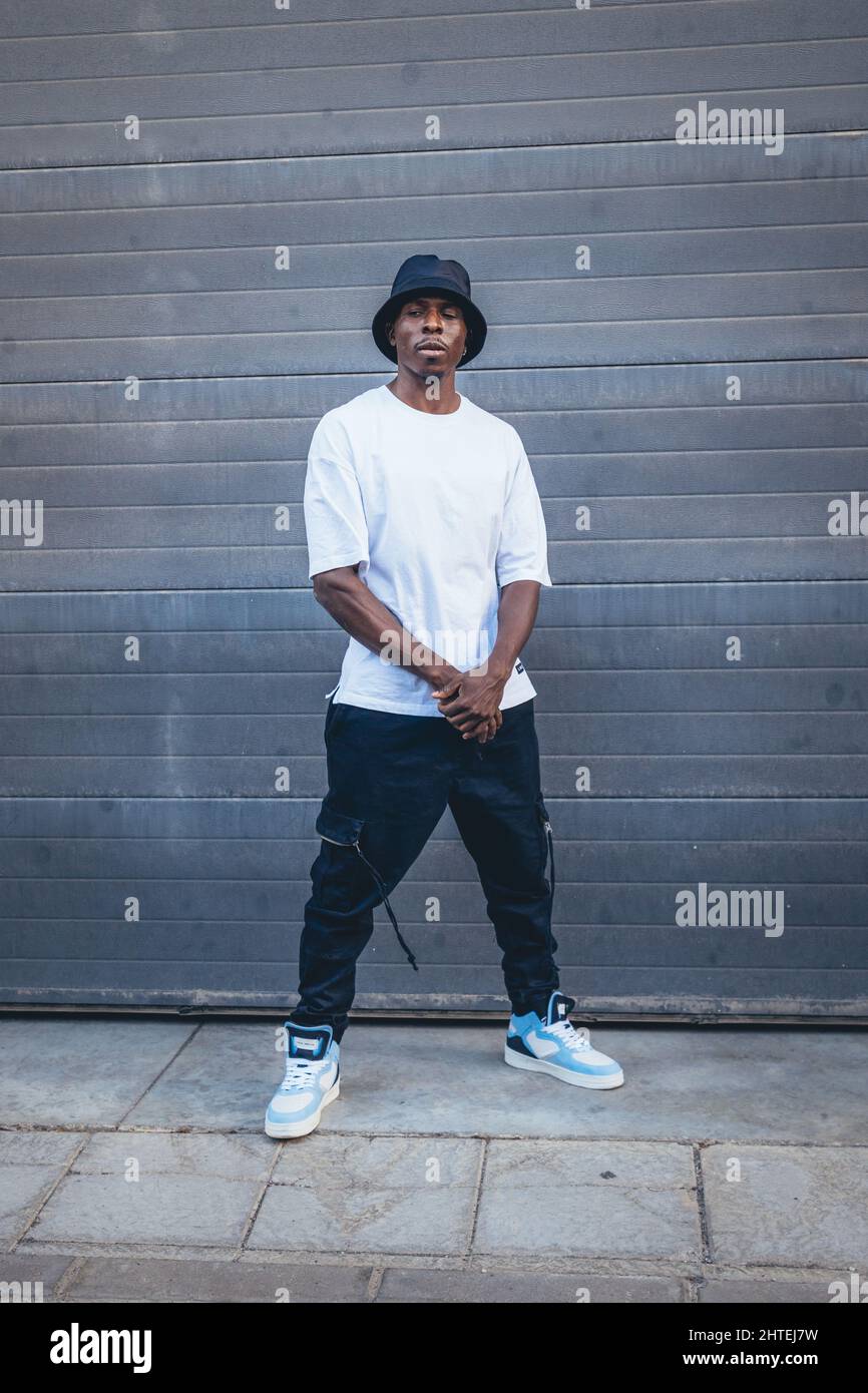 A vertical shot of a model casual young Black male with a blue hat posing in the street outdoors Stock Photo