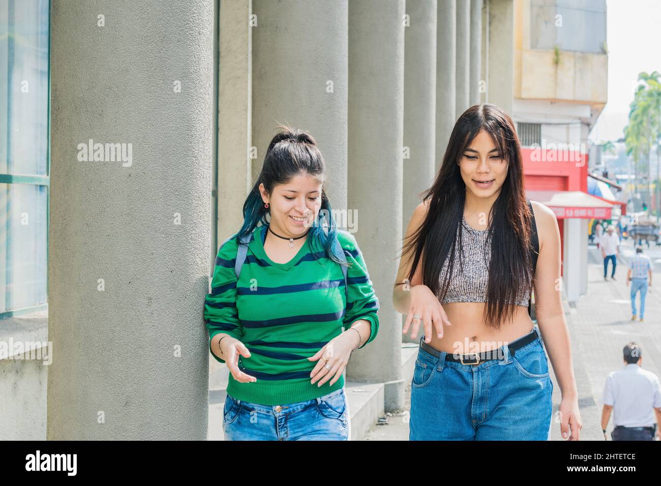 two beautiful latina girls (caucasian and brunette) walking down the street very cheerful while talking and discussing their dreams and future goals. Stock Photo