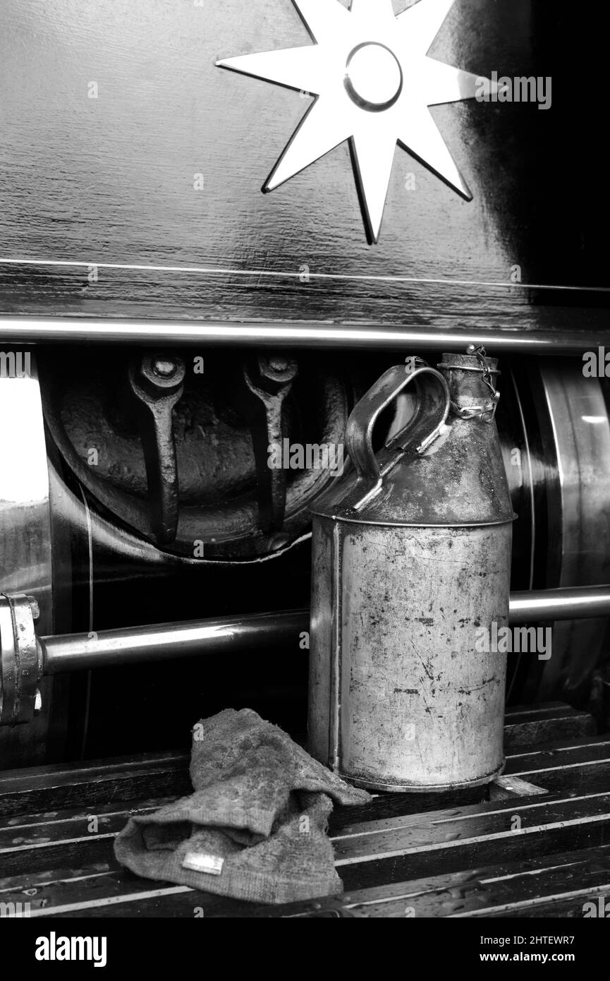 Vertical of a vintage oil canister against a farming steam engine in grayscale Stock Photo