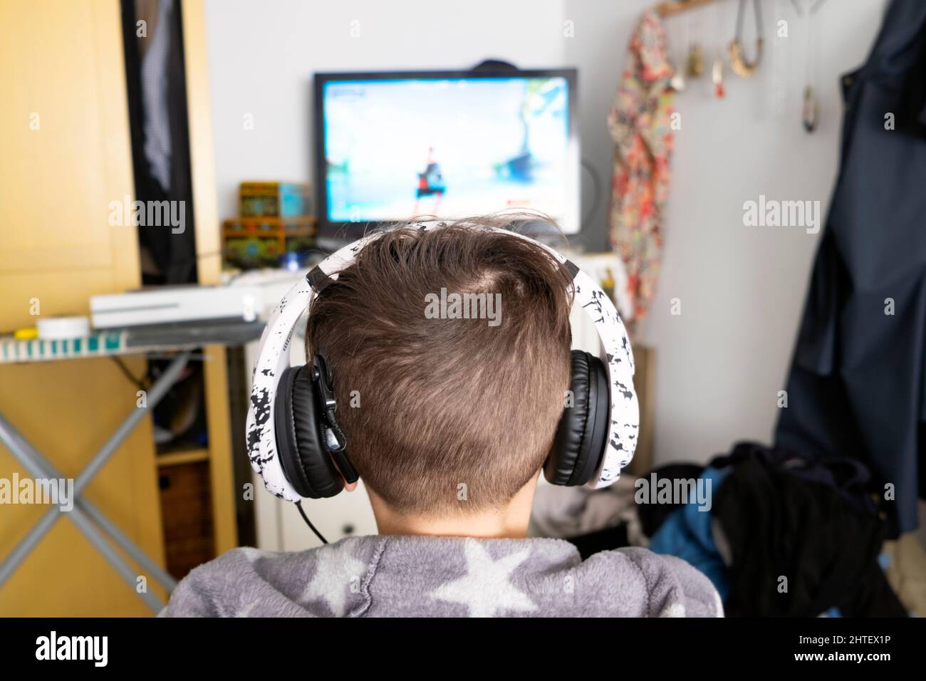 Back head faceless deaf boy child 12 years wearing headphones looking at screen playing computer game at home in bedroom UK Great Britain KATHY DEWITT Stock Photo