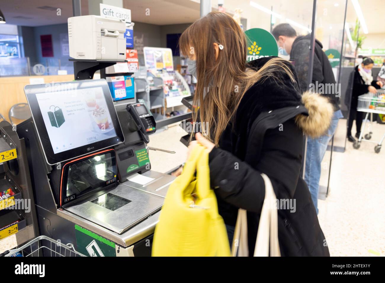 Young woman with yellow handbag paying for shopping items at self-service payment till screen in Morrisons supermarket 2022 Wales UK   KATHY DEWITT Stock Photo