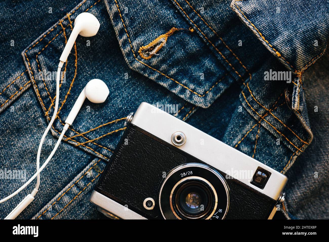 Film camera and white wired headphones lie against background of denim. Fashionable hipster background. Retro style. Photographer's Day. Top view Stock Photo