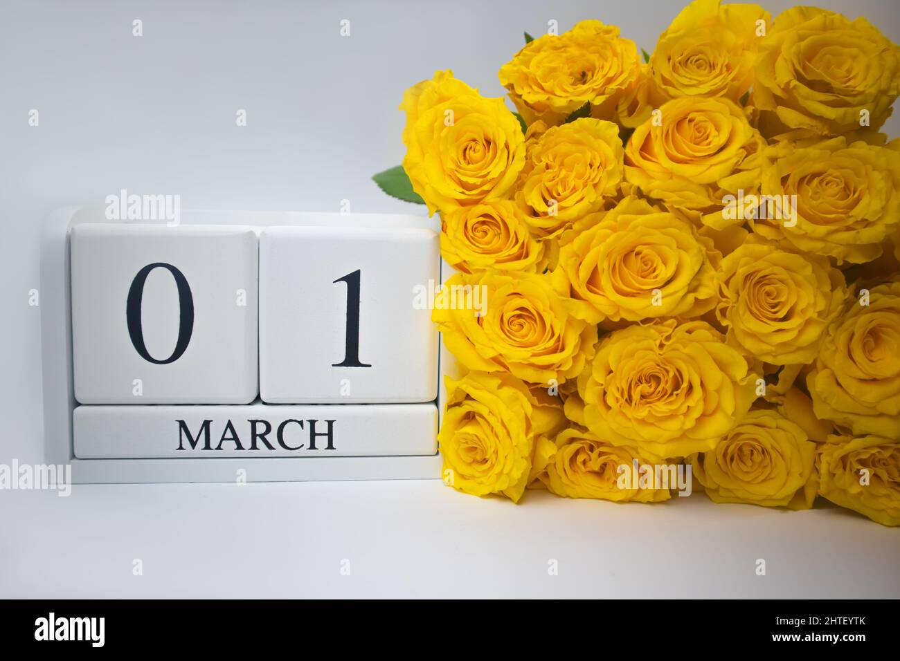 Wooden calendar March 1 and yellow roses on a white background.  Stock Photo