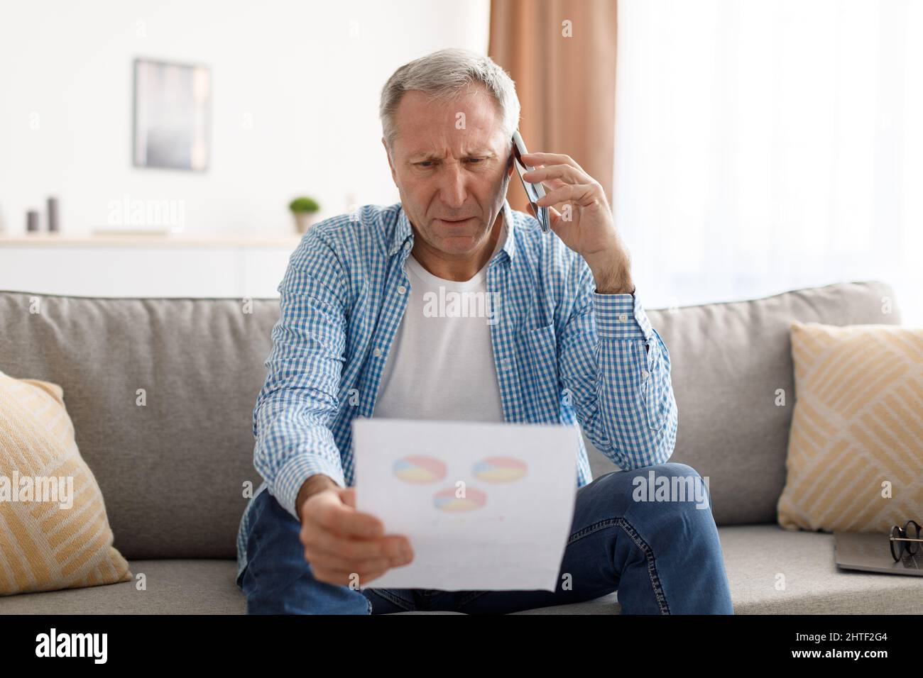 Focused mature man holding paper reading report talking on phone Stock Photo